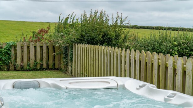 Un bain à remous dans un jardin, avec une clôture en bois et de la verdure en arrière-plan.