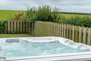 A hot tub in a backyard with a wooden fence and greenery in the background.
