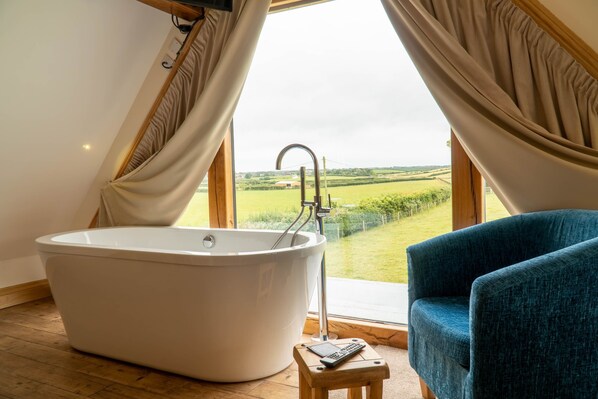 A modern bathroom with a freestanding bathtub, a wooden stool, and a blue chair. - Bluebell Cottage - Two bedroom property with hot tub, close to the beach. (Ulverston)