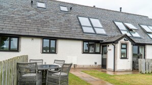 Een huis met een pannendak, een omheinde achtertuin en een terras met rieten meubilair.