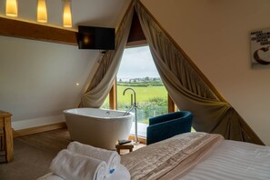 A bedroom with a large bathtub, a bed, a TV, and a view of a green landscape. - Bluebell Cottage - Two bedroom property with hot tub, close to the beach. (Ulverston)