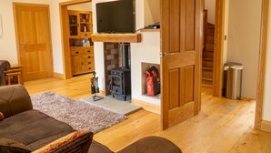 A cozy living room with a fireplace, wooden furniture, and a television mounted above it. - Primrose Cottage -  2 Bed cottage with Hot Tub, walk to the beach. (Ulverston)