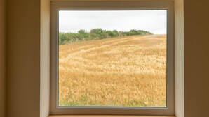 A window with a view of a golden field and a line of trees in the distance. - Primrose Cottage -  2 Bed cottage with Hot Tub, walk to the beach. (Ulverston)