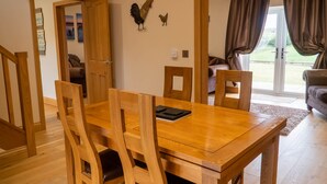 A dining area with a wooden table and chairs, a wall-mounted rooster decoration, and a view through a glass door to an outdoor space. - Primrose Cottage -  2 Bed cottage with Hot Tub, walk to the beach. (Ulverston)