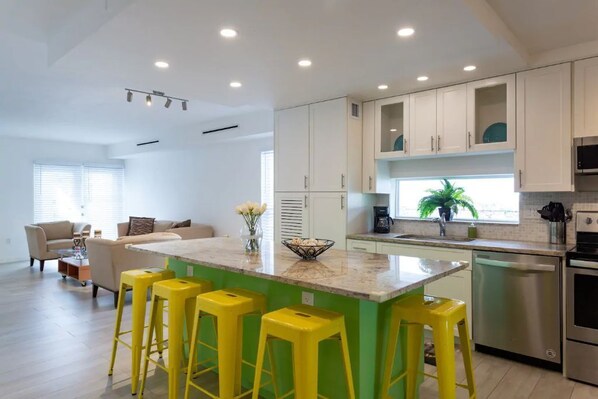 A modern kitchen with white cabinets, a green island, yellow bar stools, and a stainless steel dishwasher. - Near Beaches downtown Renovated  large  3/2  one story  townhouse  "Casa Mango " (Miami)
