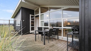 A covered outdoor area with a wooden deck, a table with chairs, and a grill.