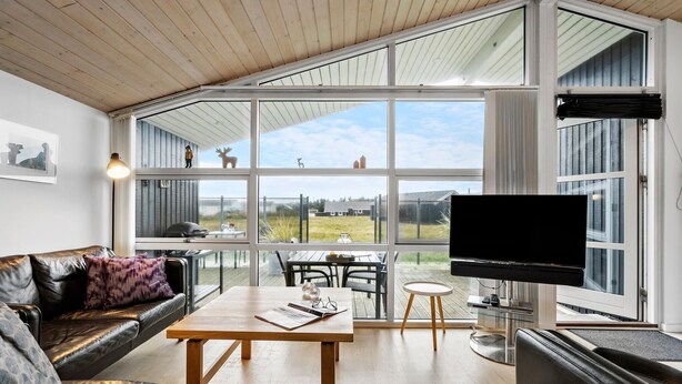 A modern living room with a large glass wall, a wooden ceiling, and a flat-screen TV.