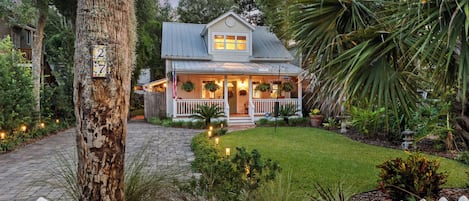 A two-story house with a porch, surrounded by a white picket fence, and a well-maintained garden.