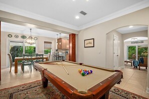 Une table de billard dans une pièce spacieuse, avec un coin repas et une cuisine en arrière-plan.