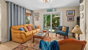 A living room with a sofa, armchair, coffee table, and a glass door leading to an outdoor area. - Casa DeSoto - Luxury Downtown Oasis (St. Augustine)