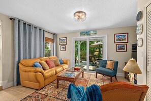Ein Wohnzimmer mit Sofa, Sessel, Couchtisch und einer Glastür zum Außenbereich.