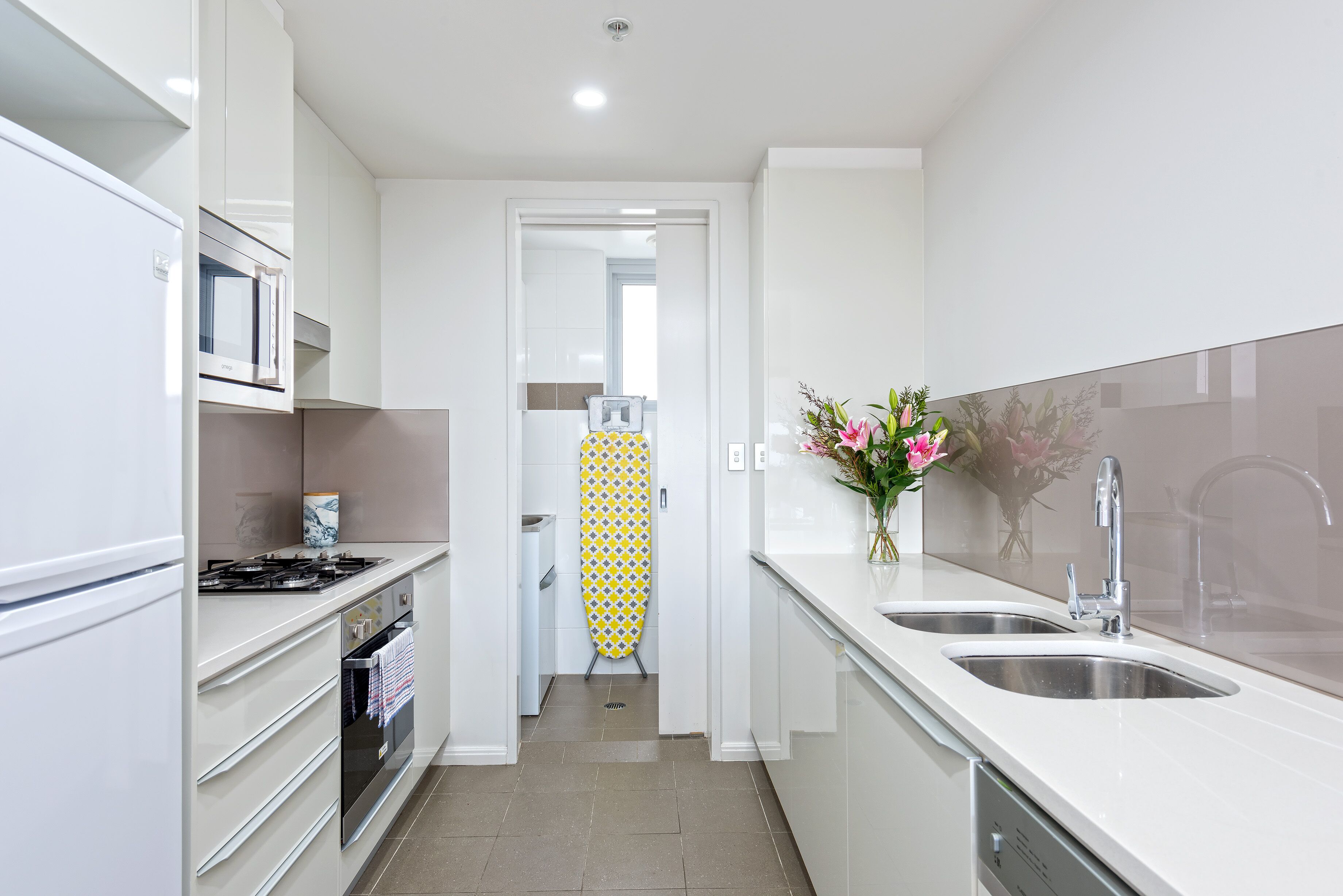 A narrow kitchen with white cabinets, a stainless steel sink, and a microwave.