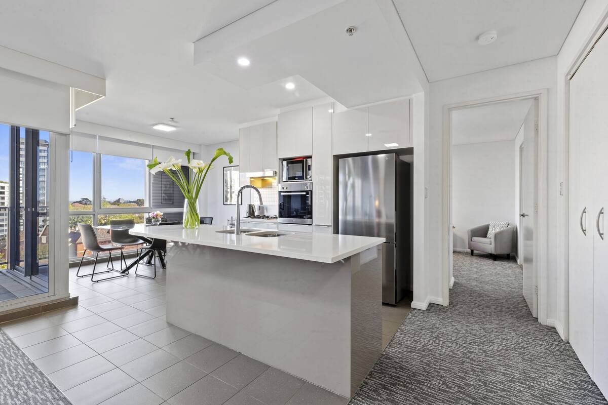 A modern kitchen with a central island, built-in appliances, and a view to the outside.