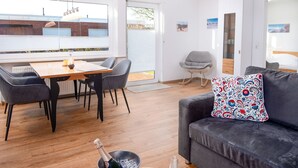 Een moderne woonkamer met een grijze bank, een houten eettafel en een grijze schommelstoel.