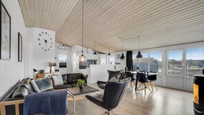 Ein modernes Wohnzimmer mit einer Couch, einem Couchtisch und einem Essbereich. Im Hintergrund befindet sich eine Küche mit Blick ins Freie.