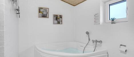 A modern bathroom with a freestanding bathtub, a showerhead, and two framed abstract paintings on the wall.