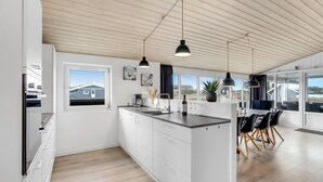 Eine moderne Küche mit weißen Schränken, einem großen Fenster und einem Essbereich mit schwarzen Stühlen.
