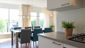 A modern kitchen with a dining area, featuring a large window, a gas stove, and a potted plant. - 3 bedroom stunning home in Vlagtwedde (Vlagtwedde)