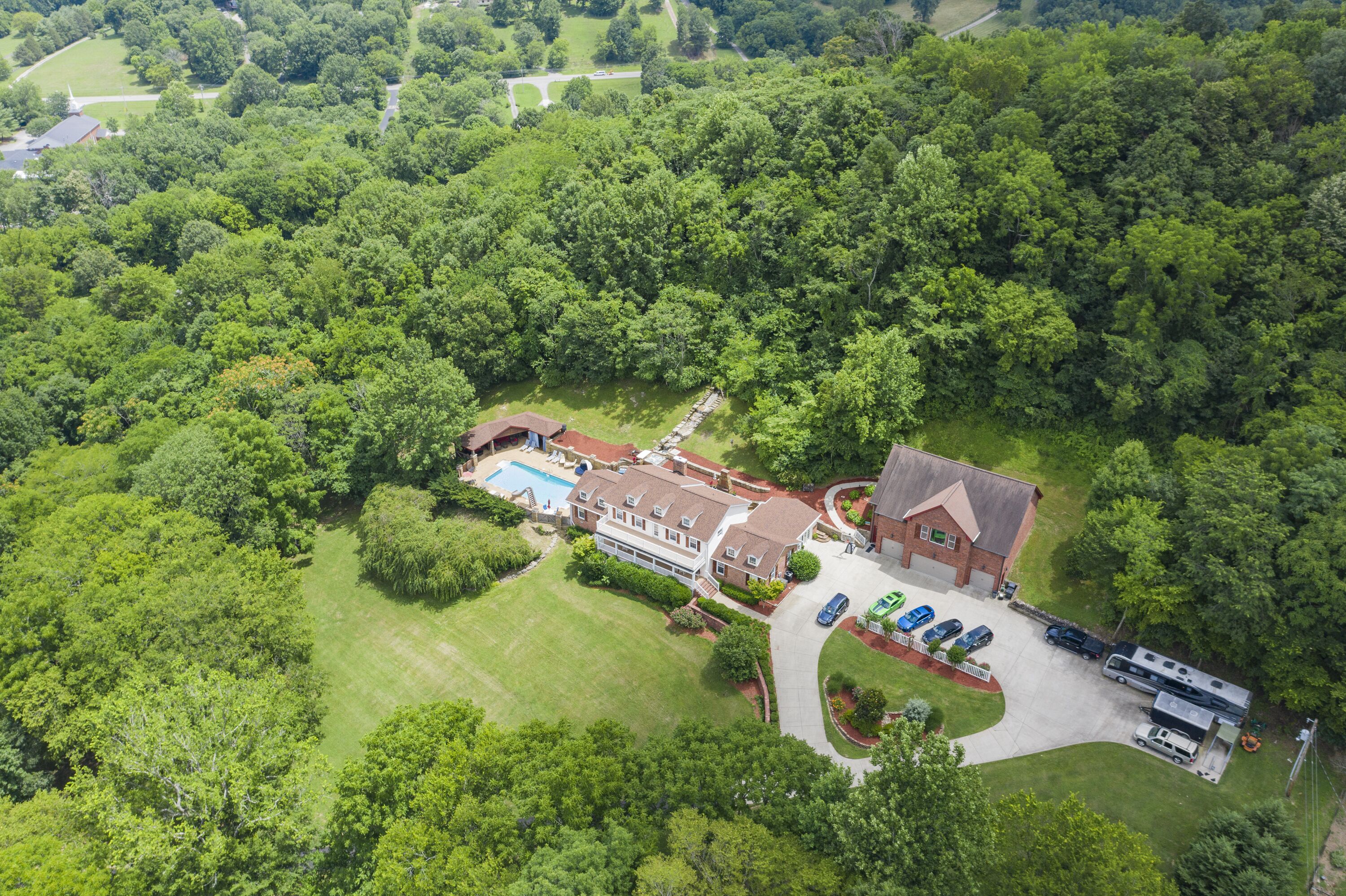 An aerial view of a large property with a swimming pool, multiple buildings, and a parking area with RVs.