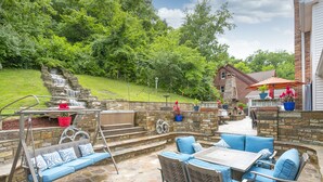 Une terrasse avec un sol en pierre, des meubles d’extérieur et une petite cascade décorative.