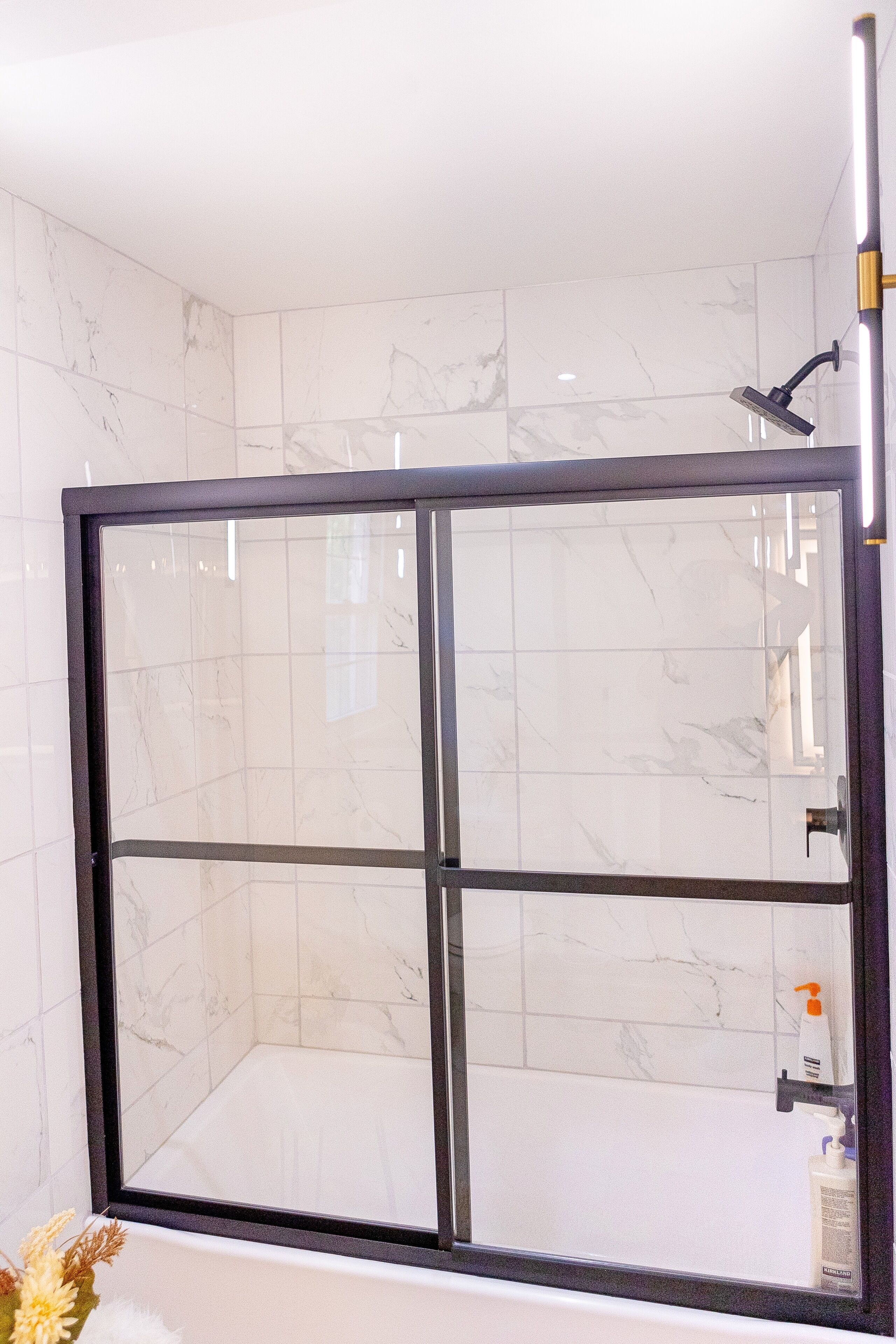 Un espace de douche doté d’une porte en verre, de carreaux de marbre blanc et d’un pommeau de douche à main.