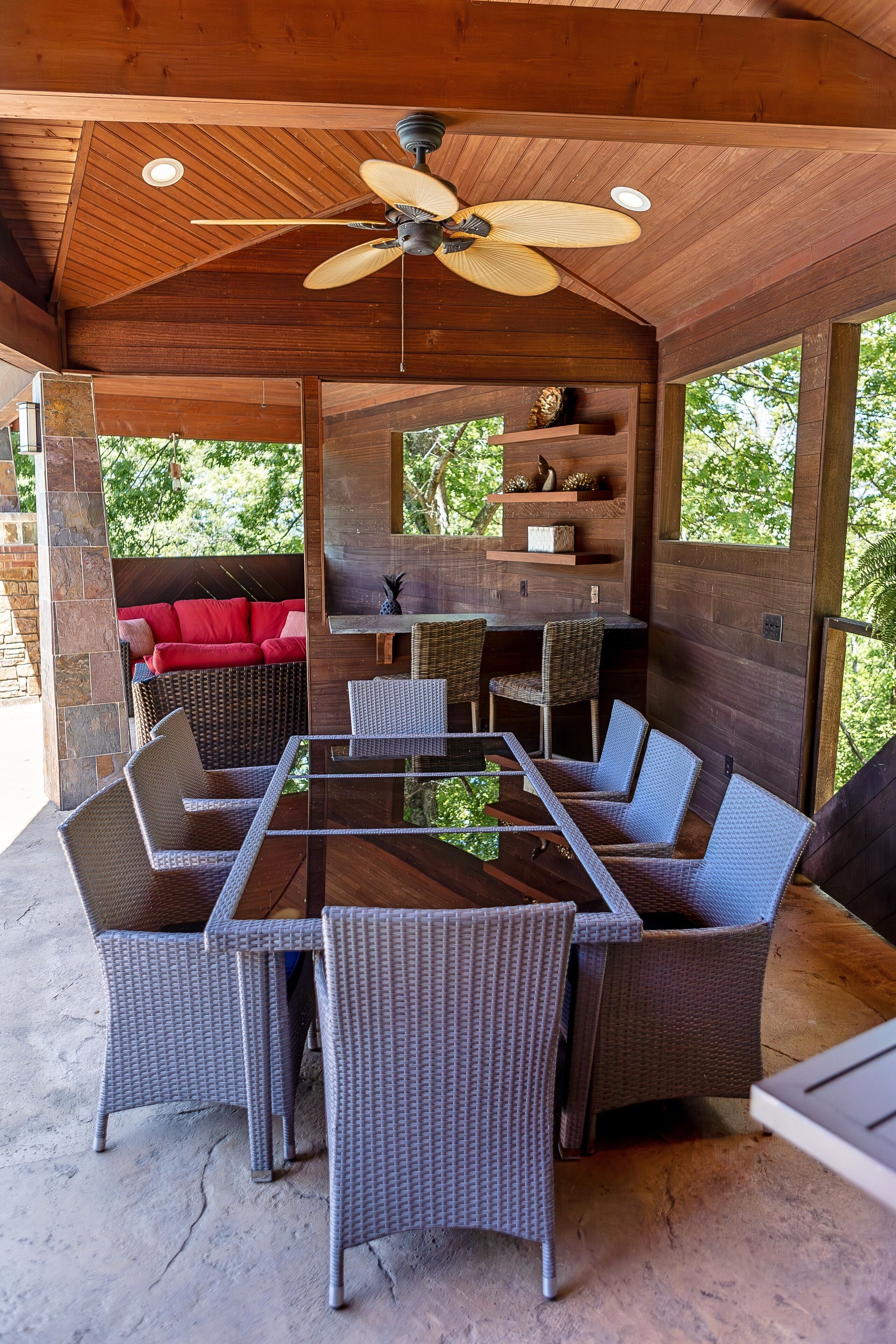 Une terrasse extérieure avec des meubles en osier, un ventilateur de plafond et un canapé rouge.
