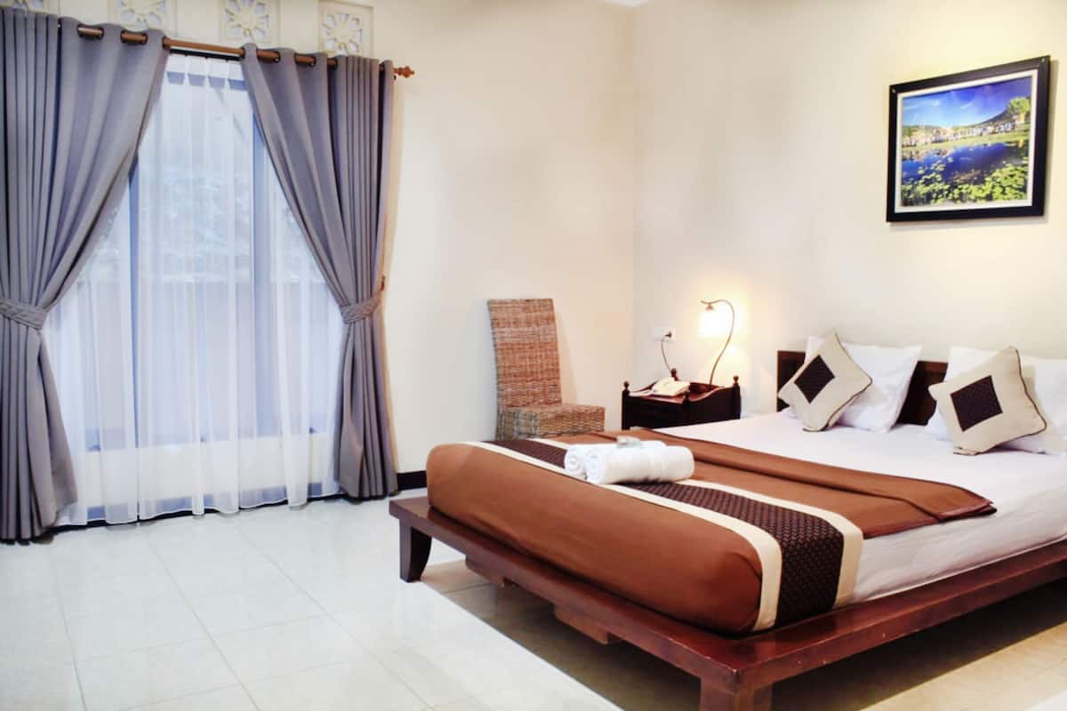A hotel room with a large bed, a nightstand, a lamp, a framed picture on the wall, and a window with curtains.