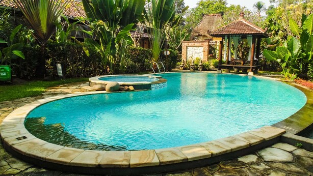 A swimming pool with a stone border, surrounded by lush greenery and a gazebo. - REVIVE Bogor Pendopo 45 Resort (Kemang)