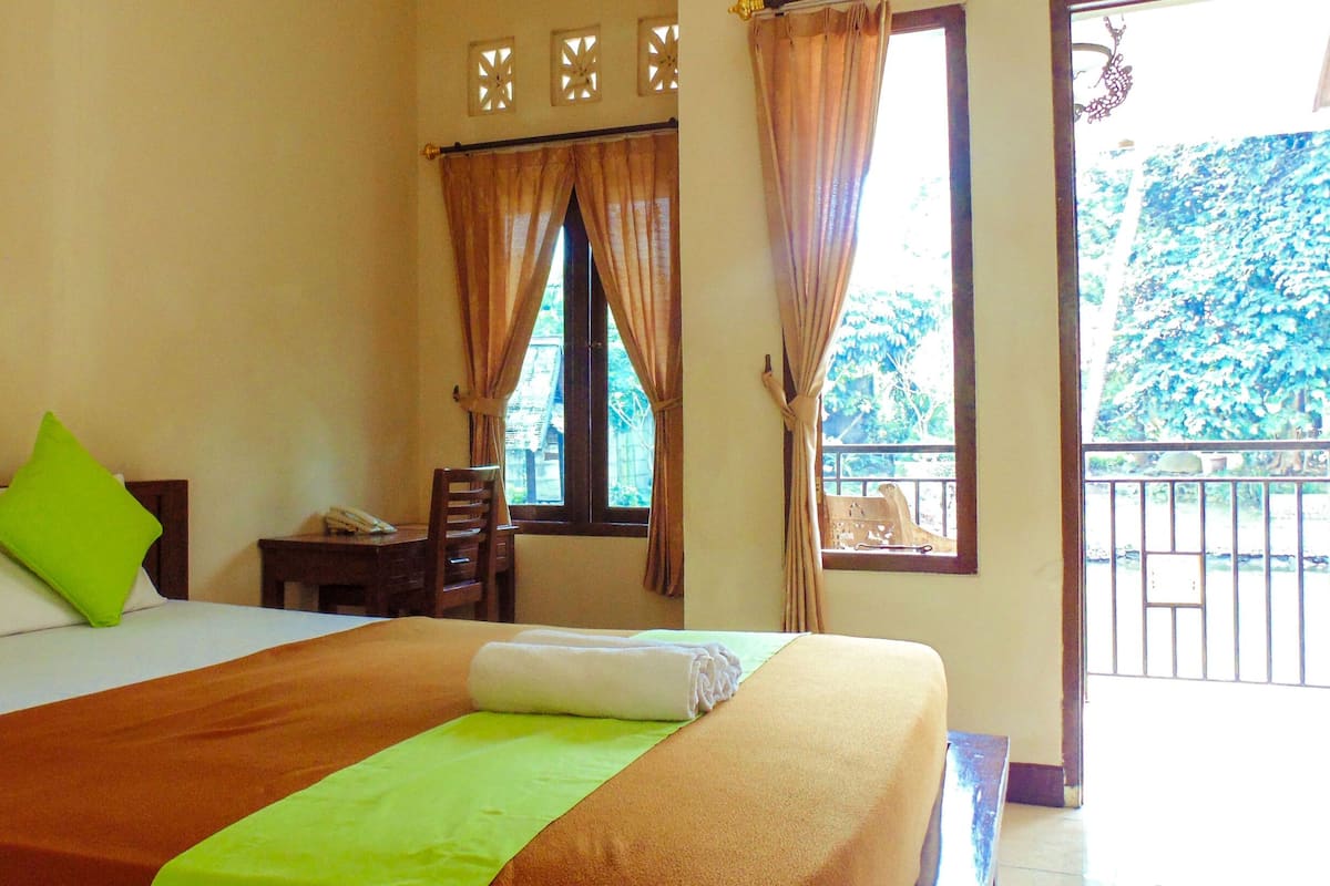 A hotel room with a bed, green pillows, a desk with a phone, and a window with curtains.