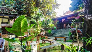 A traditional courtyard with a restaurant, a vintage motorcycle, and a staircase leading to a building with a tiled roof. - REVIVE Bogor Pendopo 45 Resort (Kemang)