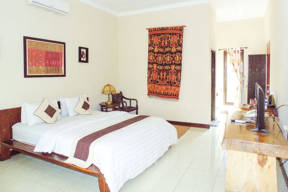 A hotel room with a bed, a desk, an air conditioner, a tapestry, and a framed picture on the wall.