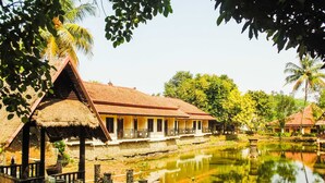 A traditional thatched-roof house with a wooden veranda, a small pond, and lush greenery. - REVIVE Bogor Pendopo 45 Resort (Kemang)