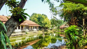A serene pond with a reflection of buildings, surrounded by lush greenery and trees. - REVIVE Bogor Pendopo 45 Resort (Kemang)