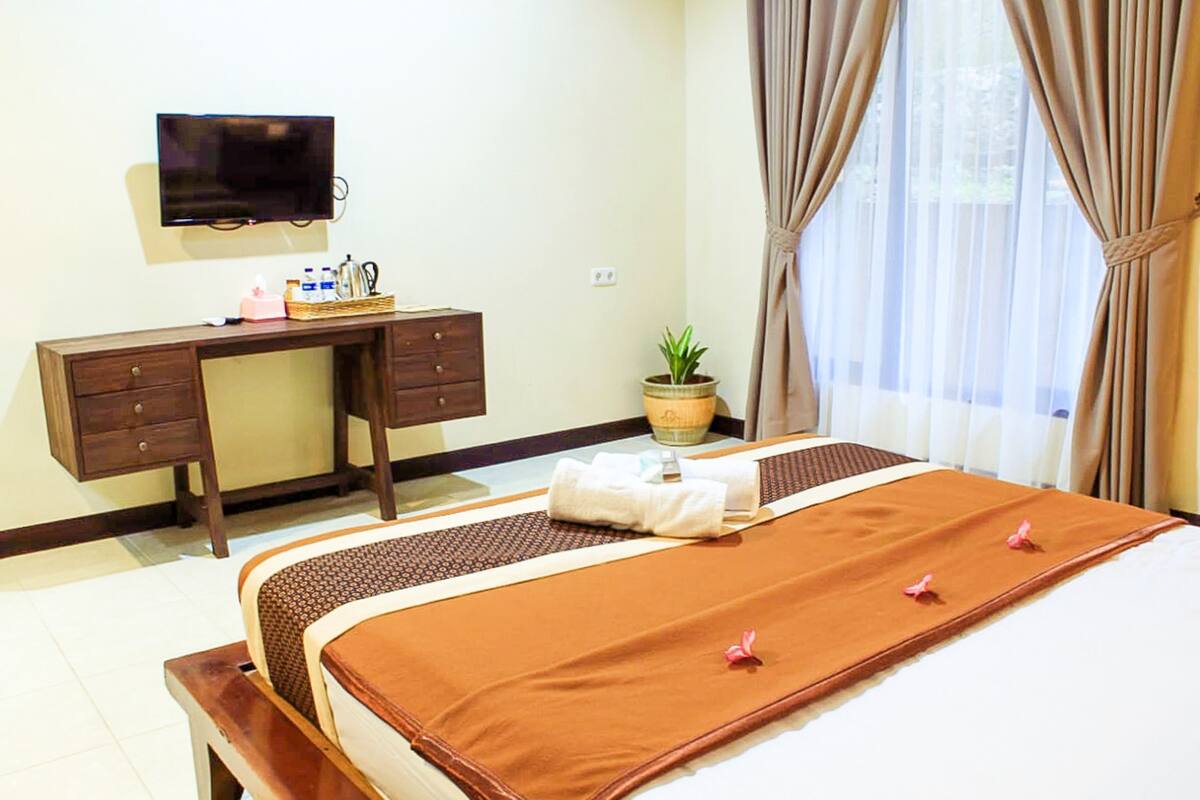 A hotel room with a bed, a desk, a television, and a window with curtains.