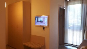 A small, narrow room with a bench, a television mounted on the wall, and a door leading to another room. - Holidayfever (Alghero)