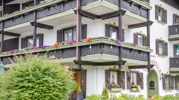 Un edificio de varios pisos con balcones decorados con flores, una cerca de madera y un letrero que indica un restaurante.