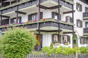 Un edificio a più piani con balconi decorati da fiori, un recinto in legno e un cartello che indica un ristorante.