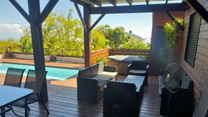 A covered outdoor area with a pool, wooden deck, wicker furniture, and a fan.
