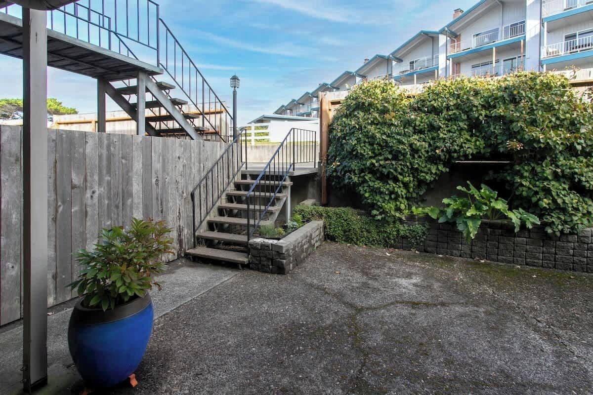 A residential area with a staircase leading to a wooden deck, a potted plant, and a building with a brick wall covered in greenery.