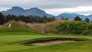 Un campo da golf con una bandiera, bunker e montagne sullo sfondo.