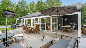 An outdoor deck with a glass-enclosed patio, wooden furniture, and a barbecue area. - 4 bedroom lovely home in Grenaa (Grenaa)