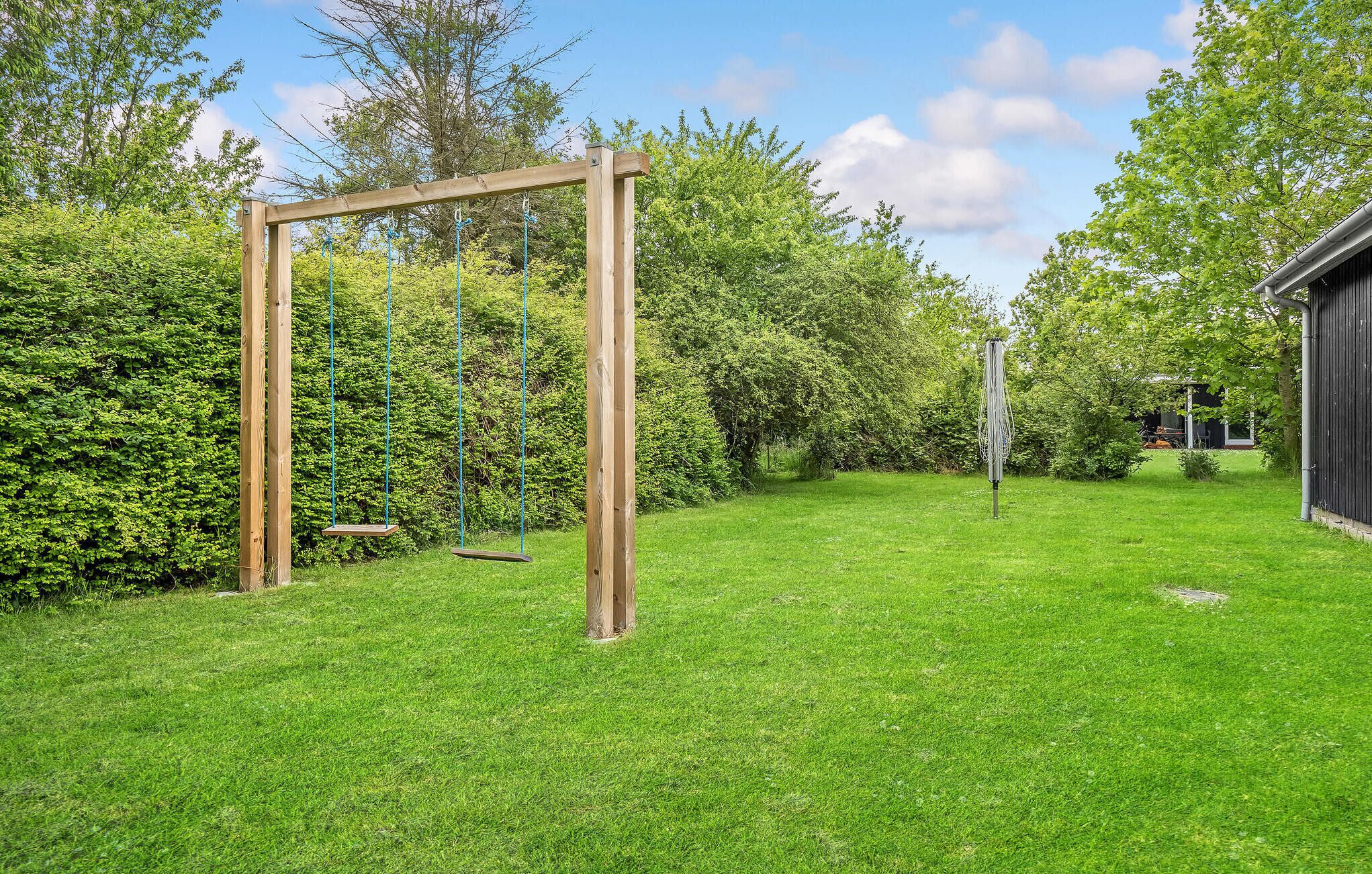 Een houten schommel in een gazon, met een haag en een tuinhuis op de achtergrond.
