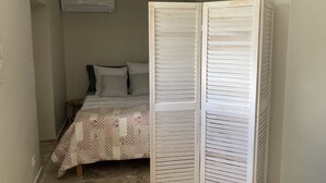 A bedroom with a bed, pillows, a quilt, a wardrobe, and an air conditioning unit. - Gîte Dipladenia with pool (Saint-Rémy-de-Provence)