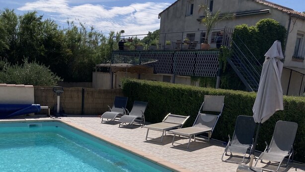 A rectangular swimming pool with clear blue water, surrounded by a tiled deck. There are lounge chairs and a covered umbrella near the pool. - Gîte Dipladenia with pool (Saint-Rémy-de-Provence)