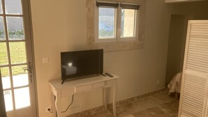 A room with a TV on a white desk, a window with blinds, and a door leading outside. - Gîte Dipladenia with pool (Saint-Rémy-de-Provence)