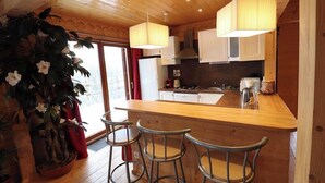 Un intérieur en bois comprenant un coin cuisine, des tabourets de bar et une grande plante en pot.
