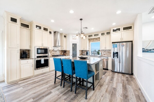A modern kitchen with light-colored cabinets, stainless steel appliances, and a central island with blue chairs.