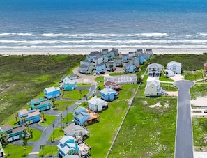 An aerial view of a coastal residential area with houses, a lighthouse, and a large white building. - Luxury Beach Retreat | Ocean Views + Elevator! (PORT ARANSAS)