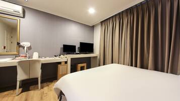 Habitación de hotel con cama, escritorio, computadora, dos monitores, secador de pelo y espejo.