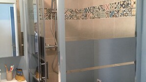 Moderni kylpyhuone, jossa on lasiseinällä varustettu suihku, pesuallas ja wc.